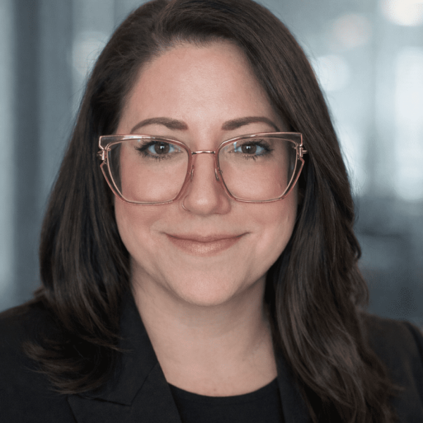 Professional headshot of a woman with glasses wearing a black suit.
