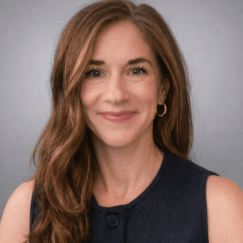 Professional headshot of a smiling woman with long brown hair wearing a navy top.